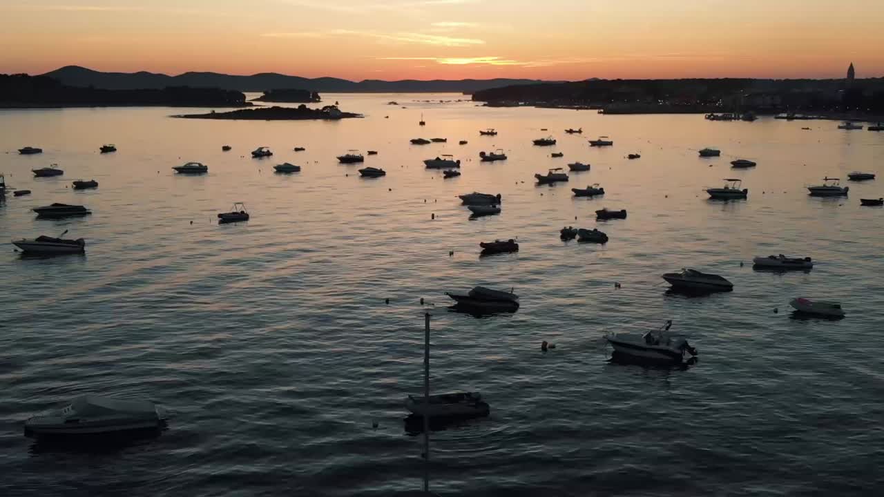 Drohnen-Dolly-Aufnahme einer Küstenlinie mit Booten im Wasser und Sonnenuntergang im Hintergrund