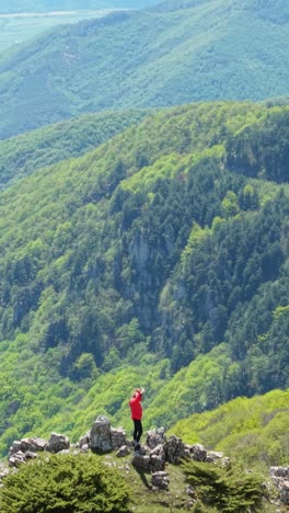 vertical aerial of a woman navigating rocky terrain in the balkan mountains. captured during spring with clear skies, nature in bloom, and mountain views.