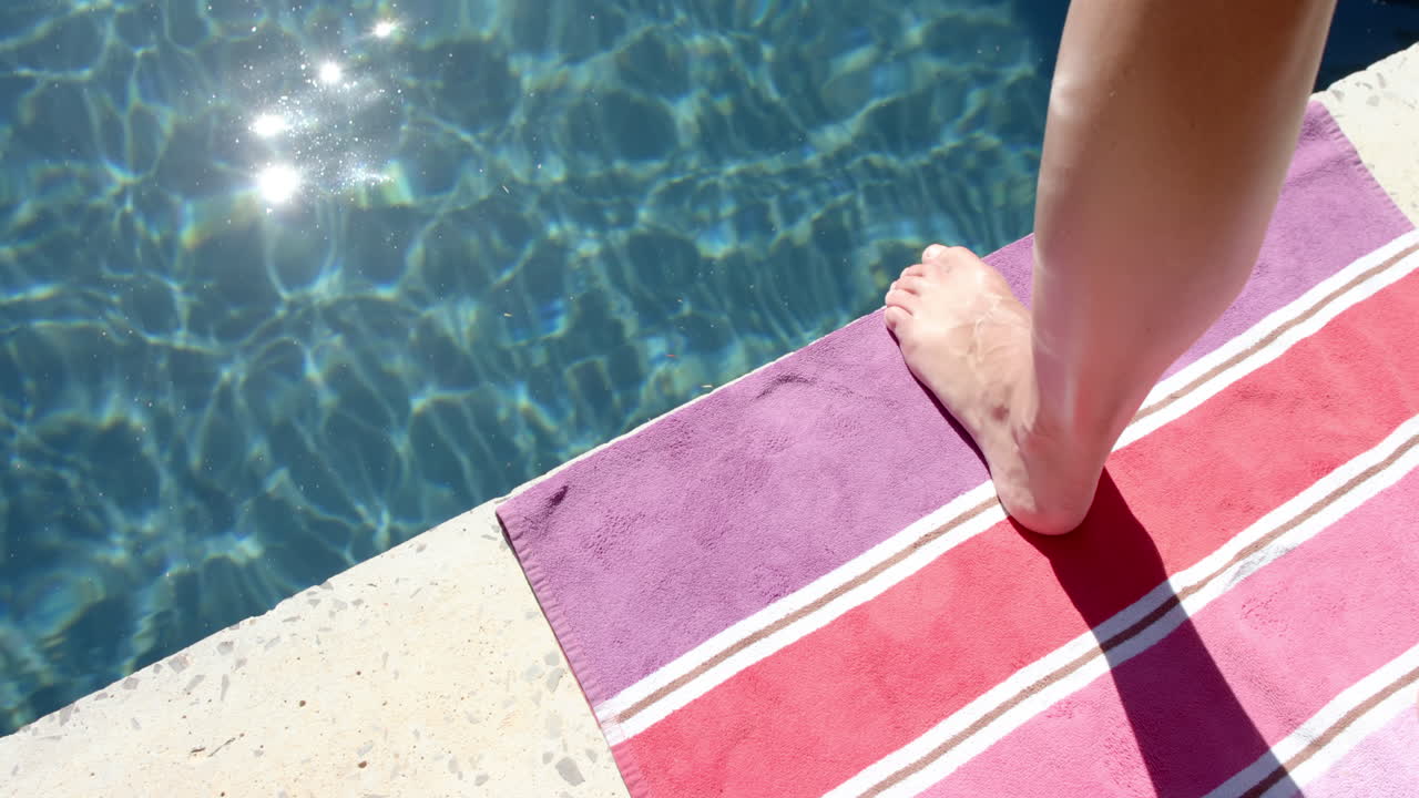 Barfüßige Person steht auf einem rosa Handtuch an einem funkelnden Pool mit Textfreiraum