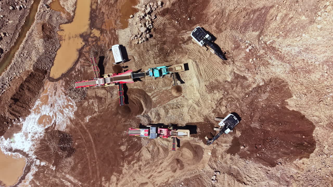 Construction equipment operates on a site with soil and rock removal taking place in a mining area during daylight hours