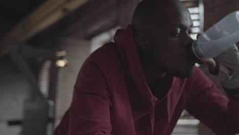 boxador africano cansado con capucha apoyándose en cuerdas y agua potable