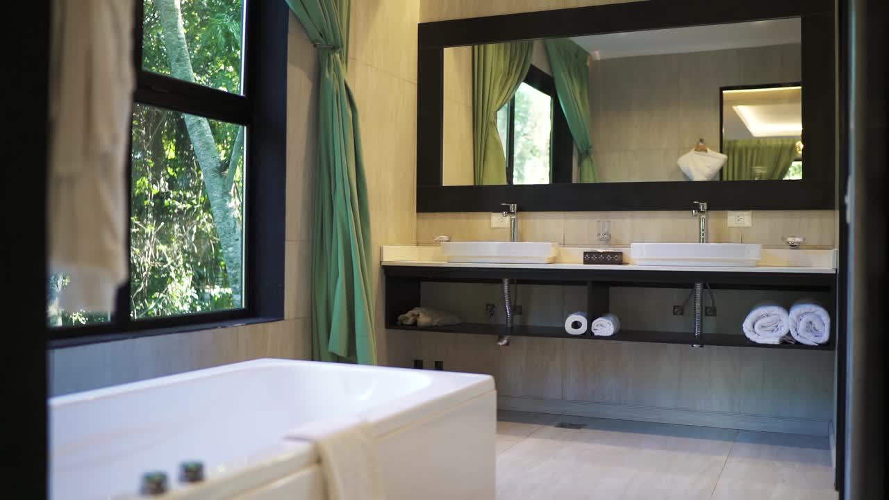 Interior panning clean hotel bathroom in the woods, mirror, bathtubs around greenery