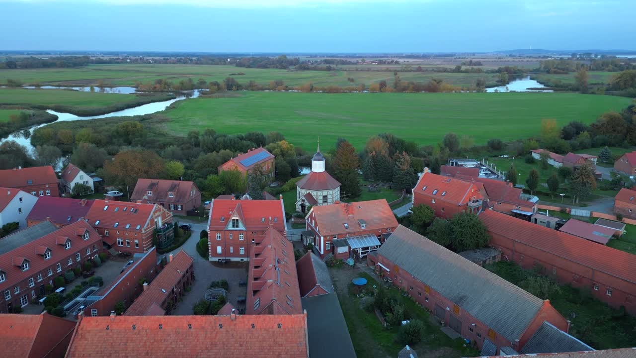 a small village illuminated by golden hour light, casting long shadows over the surrounding fields. Amazing aerial view flight drone shot footage from above
