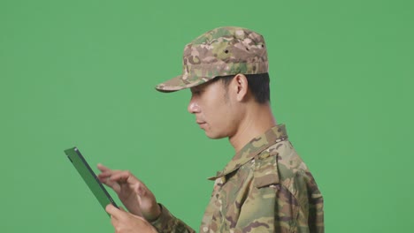 close up of side view asian man soldier using a tablet while walking in the green screen background studio