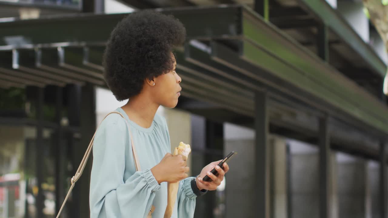 African american businesswoman eating and using smartphone