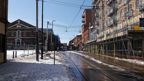 People-crossing-street-near-tram-lines-on-sunny,-snowy-day,-Sheffield