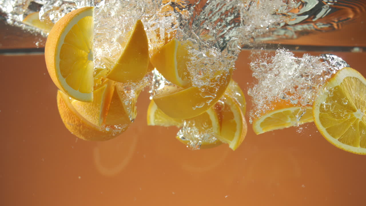 Slow motion of fresh sliced Oranges falling into water on orange background