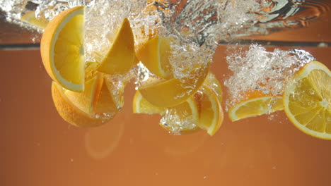 cámara lenta de naranjas frescas en rodajas cayendo al agua sobre fondo naranja