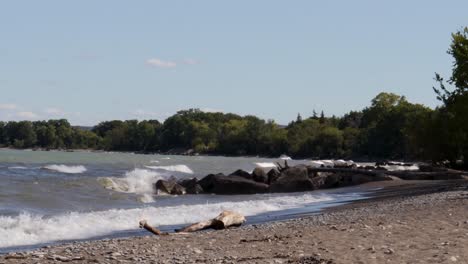 waves gently crashing along a rocky shoreline, from left to right, with lots of blue sky visible