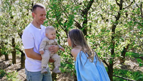 parents with their lovely baby boy in the garden. kid drops the badge and mom picks it up playing with her son.