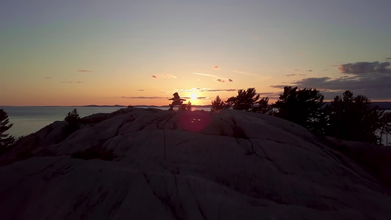 revelación de inukshuk en la isla de pinos rocosos al atardecer, antena de dron amplia rodante fuera