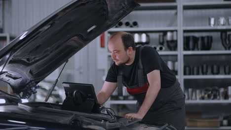 Diagnostics-of-the-car-standing-at-the-hood-in-the-car-service.-A-mechanic-in-a-close-up-car-service-holds-a-tablet-in-his-hands-and-presses-the-screen