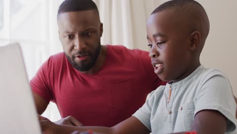 African-american-father-helping-son-to-use-laptop-while-sitting-at-home