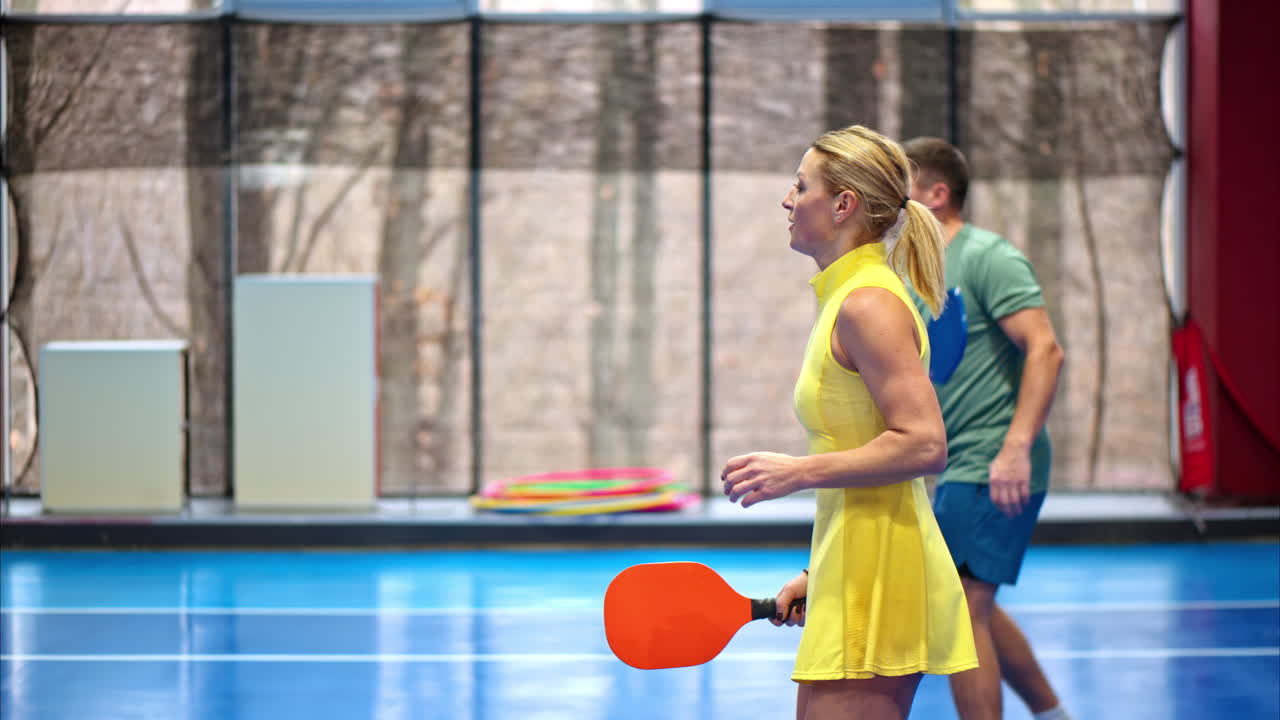 A man and a woman playing pickleball on a blue, inside court