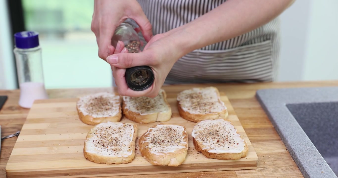 Woman sprinkles pepper over toasts topped with creamy cheese