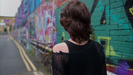 outdoor fashion portrait of young alternative style woman turning around and smiling walking along graffiti covered walls of london city street uk in real time 2