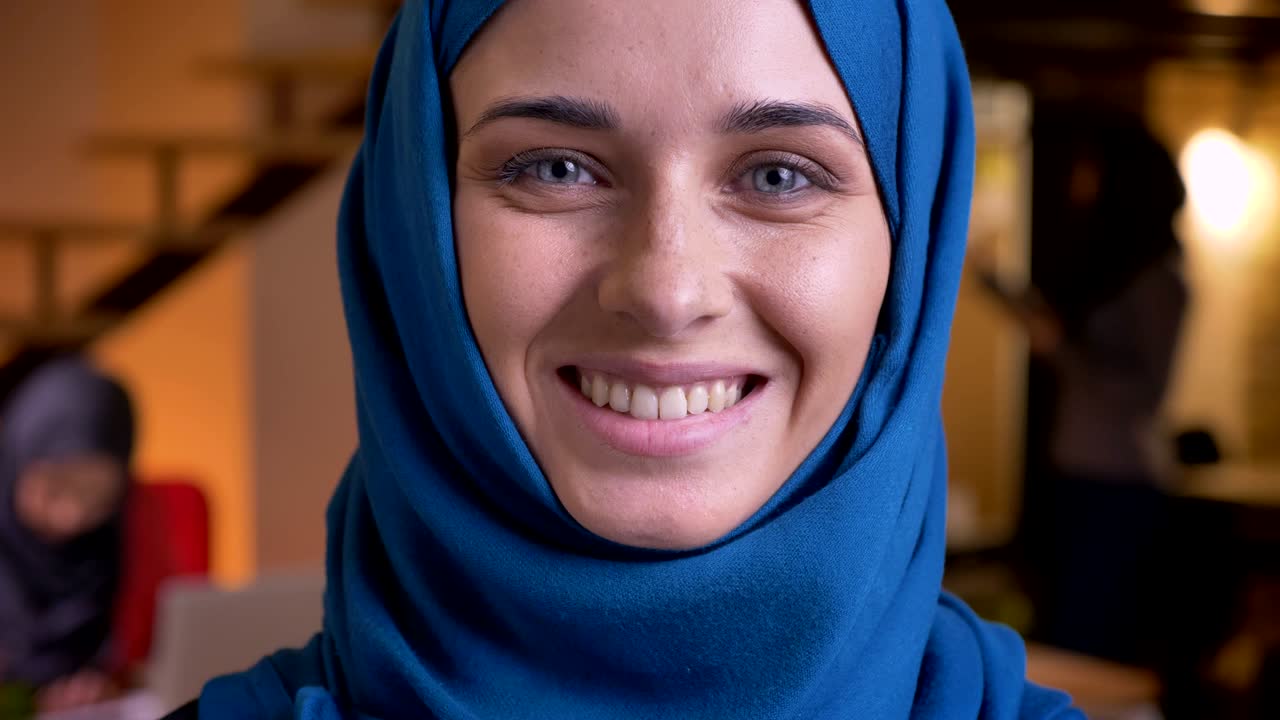 retrato en primer plano de una joven mujer de negocios musulmana con hijab azul sonriendo y mirando directamente a la cámara con sus hermosos ojos grises