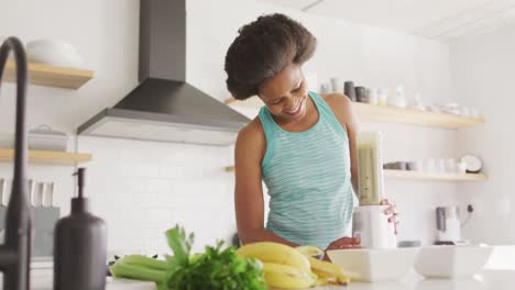 happy african american woman preparing healthy drink in kitchen