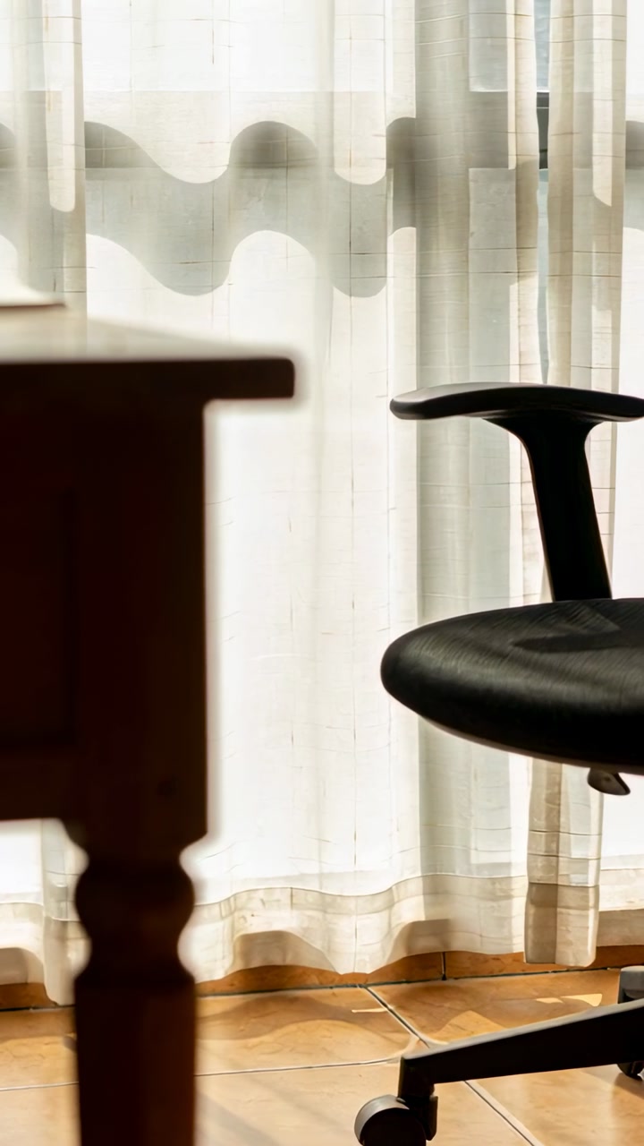 Vertical video: Showing black chair at room corner as camera pan and breeze revealing desk sheers