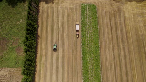 Two-tractors-on-a-hay-field,-picking-up-bales,-aerial-top-down-view