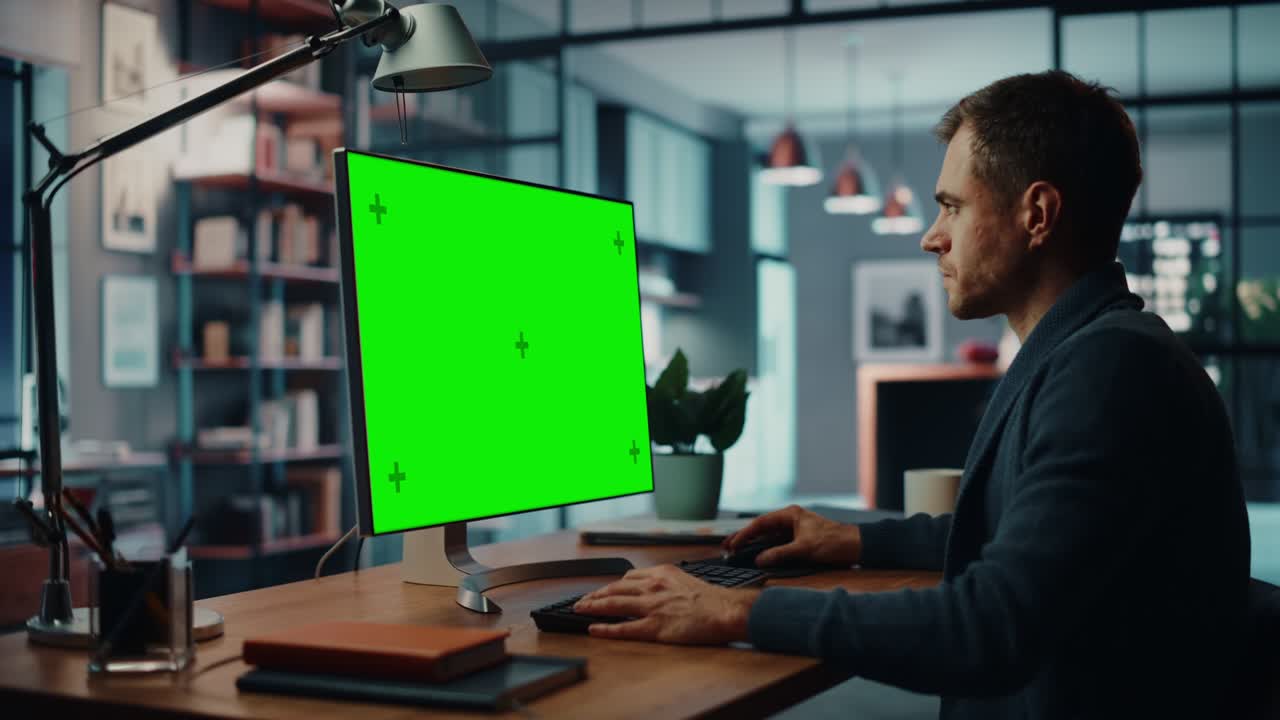 un guapo especialista caucásico trabajando en una computadora de escritorio con una pantalla verde en la sala de estar de su casa. un hombre independiente hablando con clientes a través de internet en redes sociales.