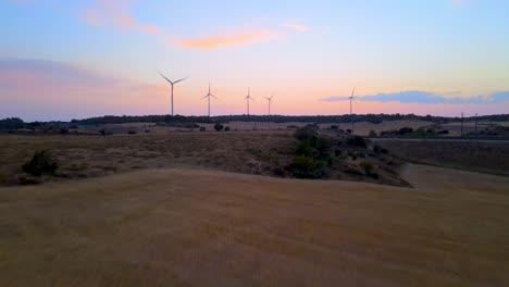 Grandes-Turbinas-Eólicas-En-Campo-De-Trigo-Vista-Aérea-Puesta-De-Sol-Naranja-Brillante-Cielo-Azul-En-El-Campo-Español-Mostrando-Ave-Tren-De-Alta-Velocidad