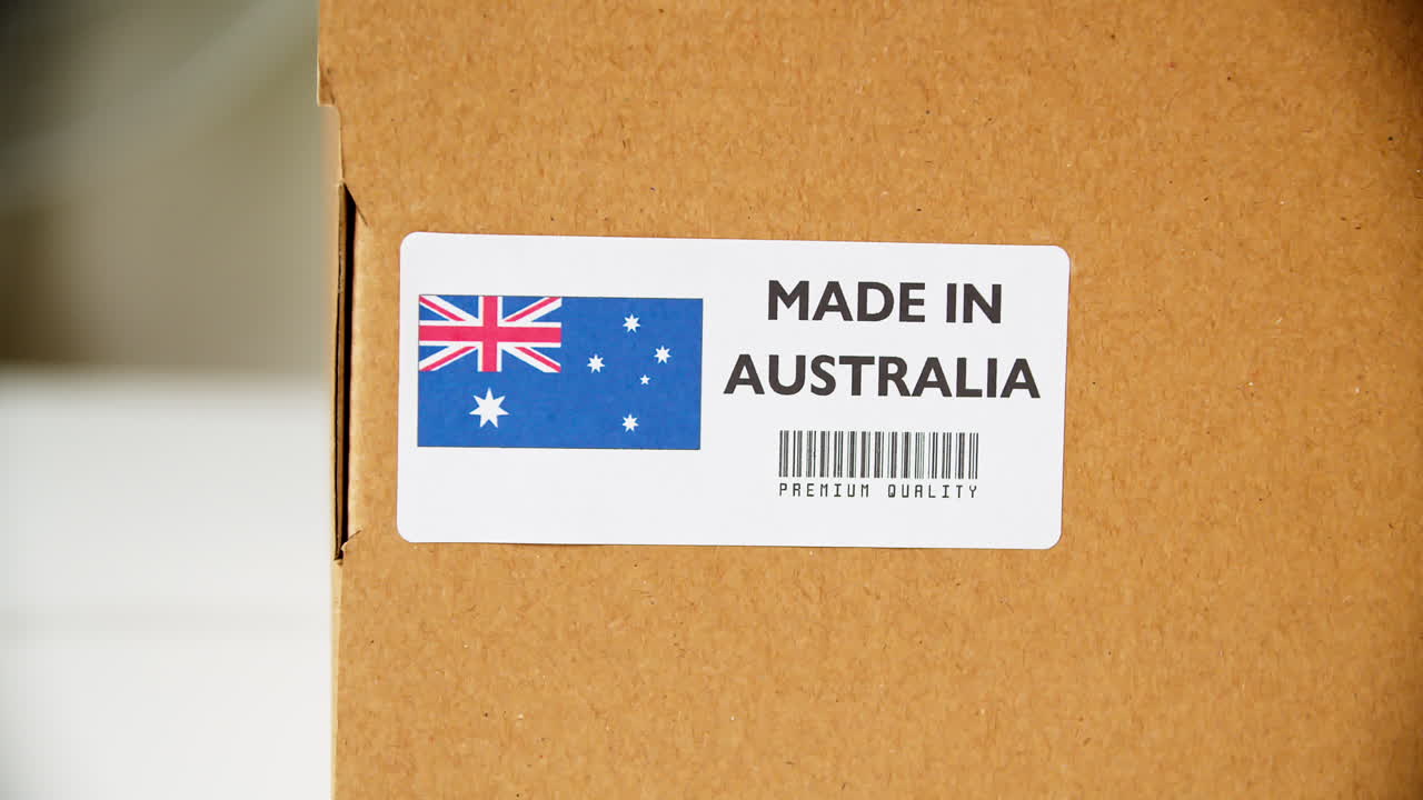 Hands applying MADE IN AUSTRALIA flag label on a shipping cardboard box with products