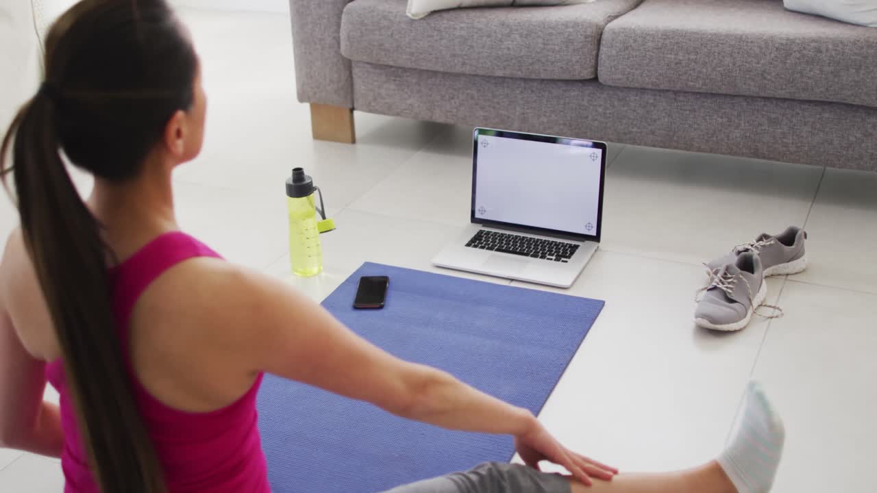 vista posterior de una mujer asiática en un tapete haciendo ejercicio con una computadora portátil con espacio de copia en la pantalla en casa