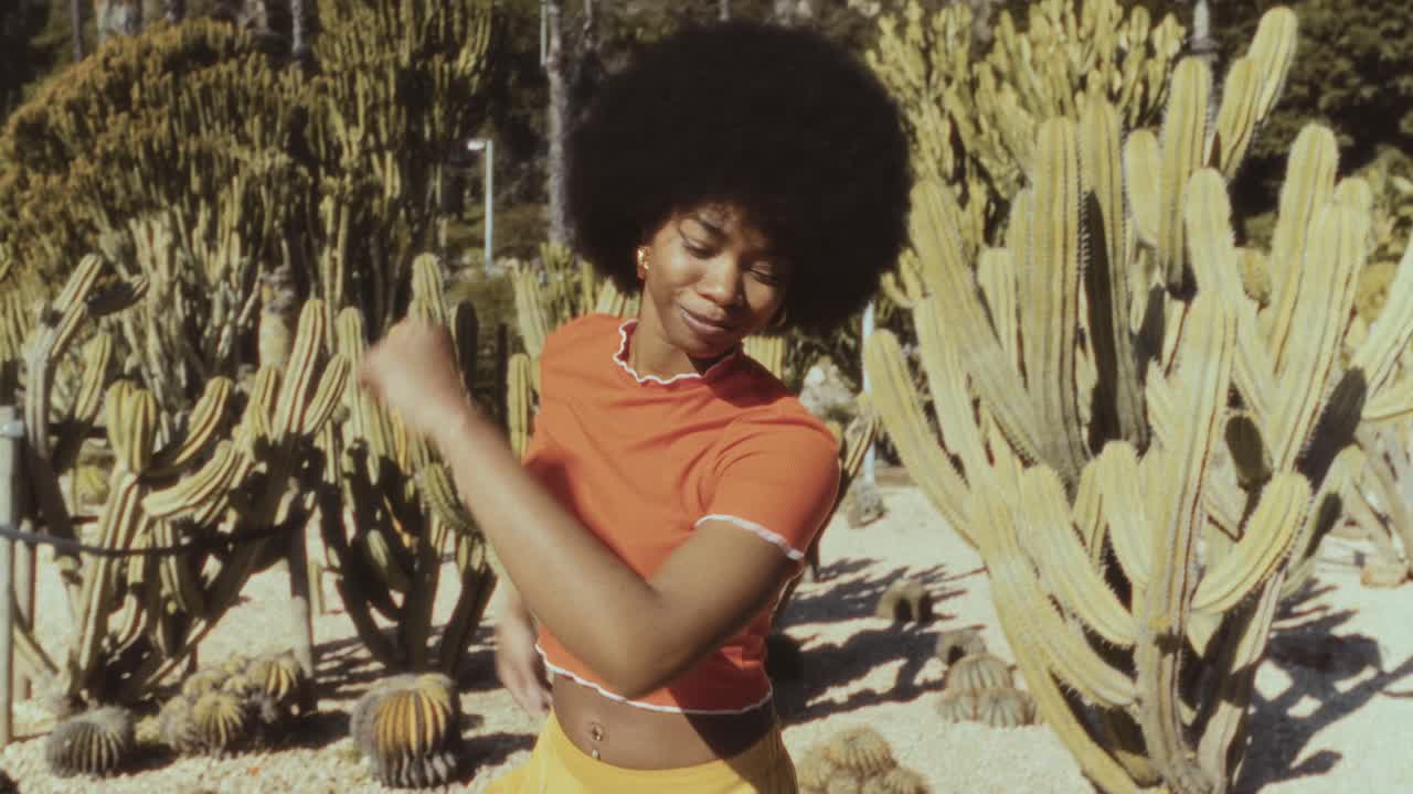 Giovane donna nera felice che balla in un giardino di cactus