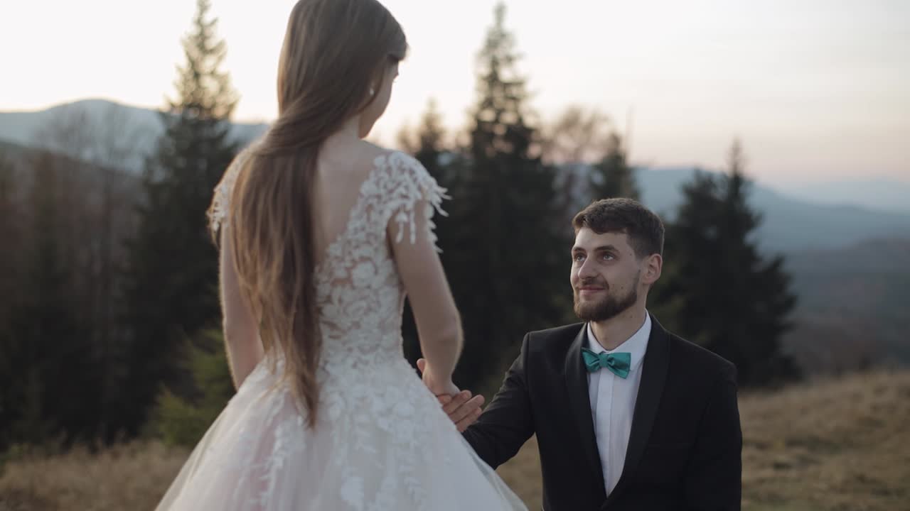 Newlyweds. Caucasian groom with bride on mountain slope. Groom proposes