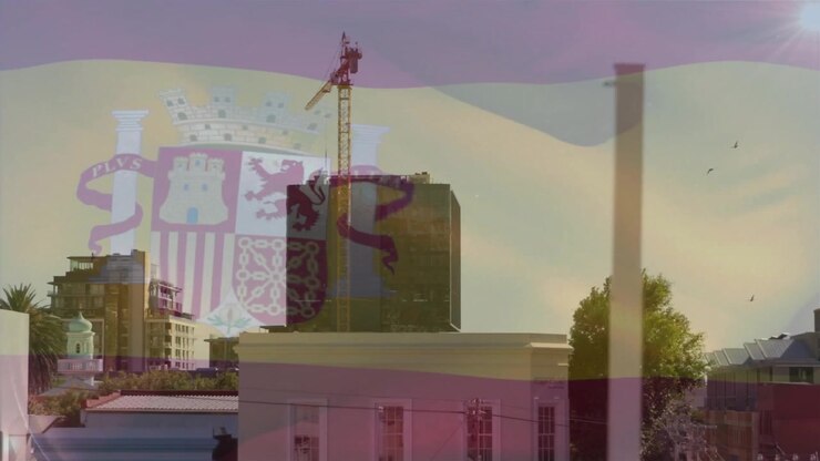Brisa iniciando sobreposição de bandeira ondulando sobre telhado central de edifício de média altura e guindaste, revelando brasão.