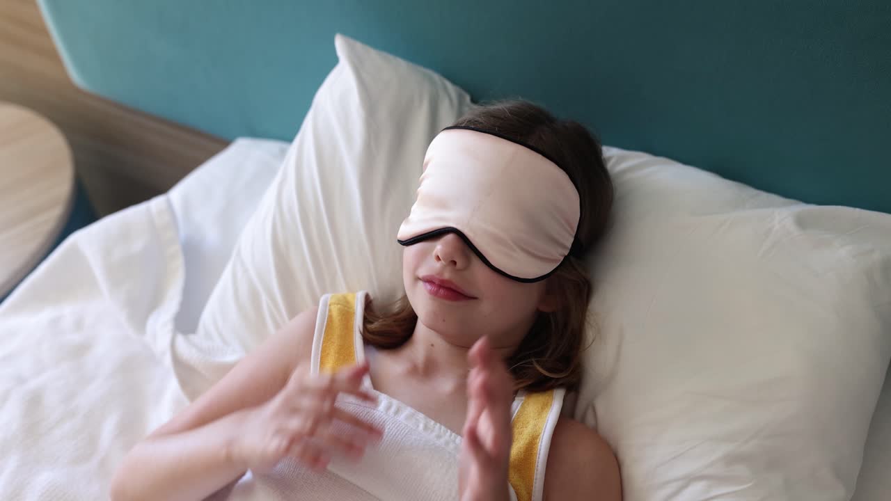 Young girl in bed with a sleep mask, appearing to wake up or rest