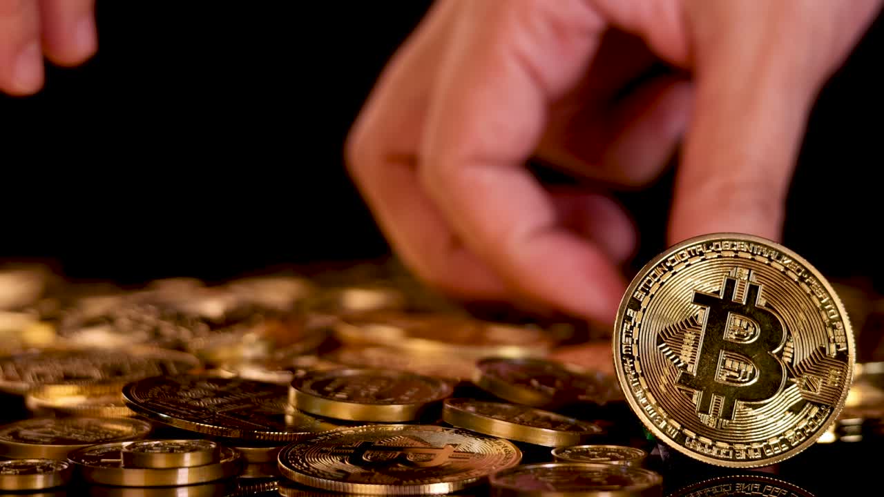 Human hand moves and stacks gold digital currency coins under dramatic studio lighting, close-up view