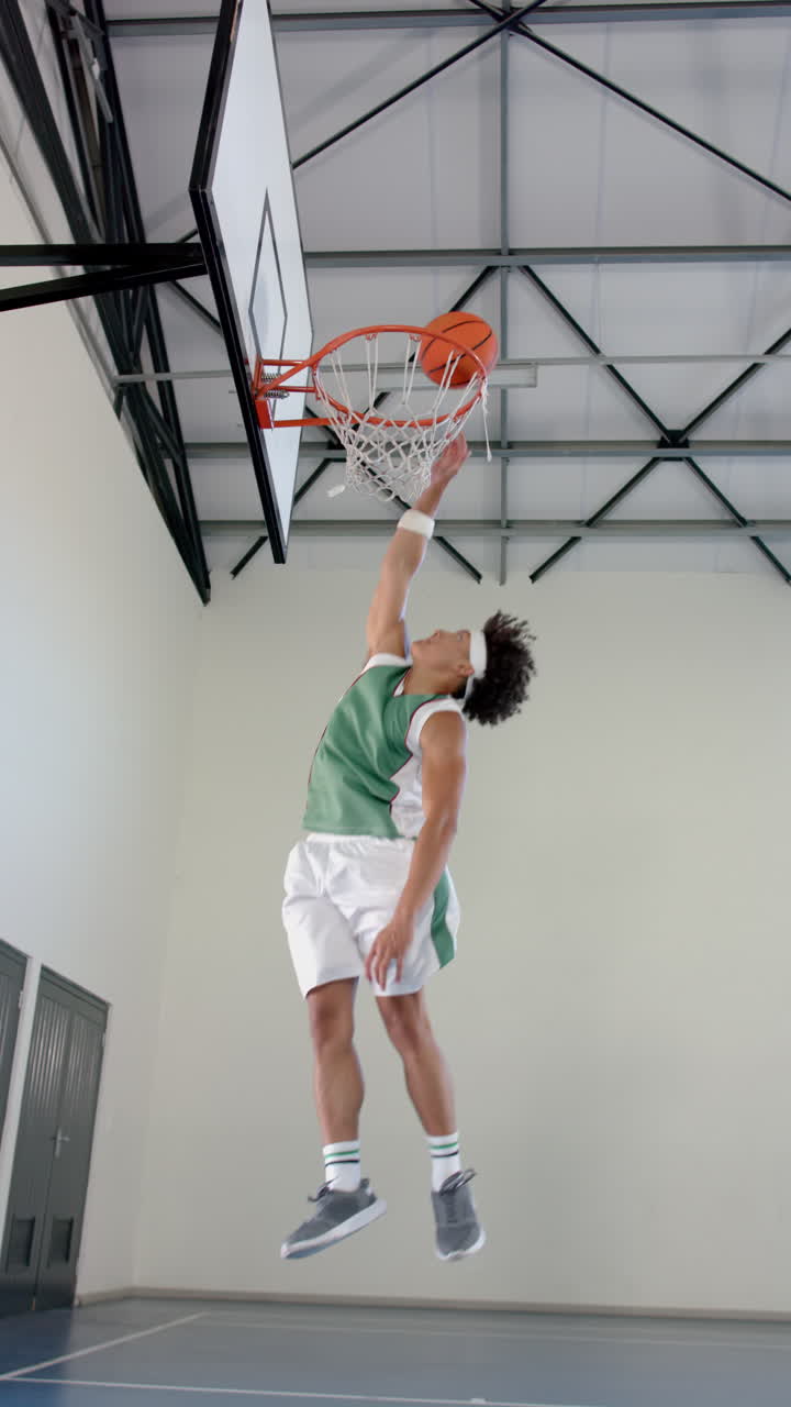 Vertical video: Playing basketball, male athlete jumping to score basket in gymnasium