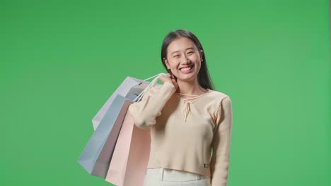 una mujer de compras asiática sosteniendo bolsas de compras siendo feliz y sonriendo a la cámara mientras está de pie frente a la pantalla verde