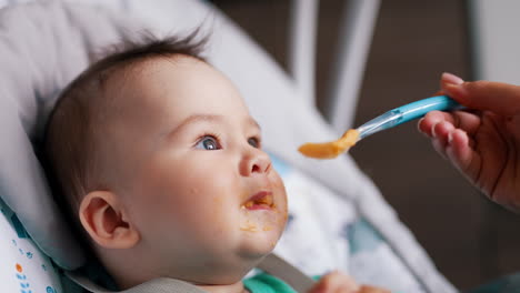 healthy little baby boy being active during meal. mommy gives her son some food and child rises hands and waves them.