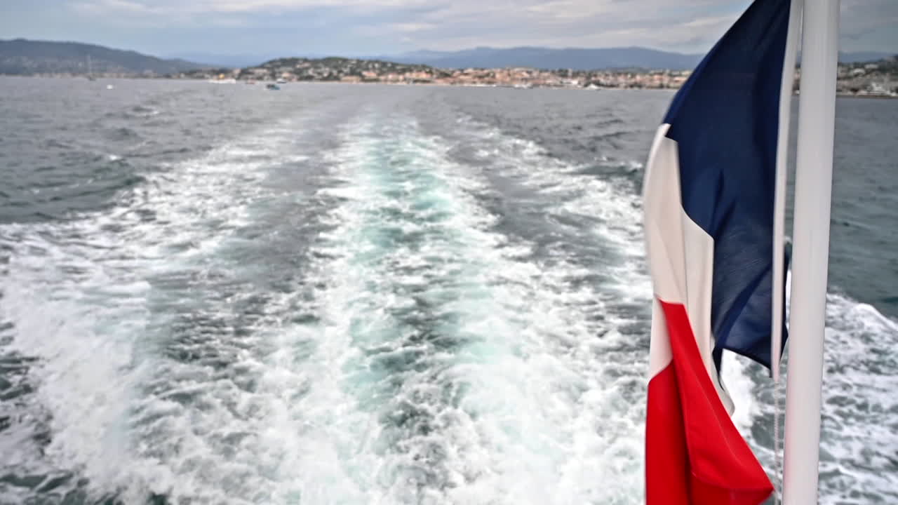 The French flag fluttering in the wind on a floating boat. Cannes in the distance. France. Slow motion