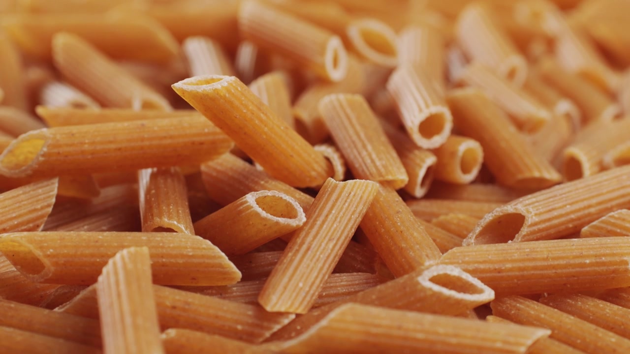 Pasta integrale biologica, maccheroni di semola di grano duro, penne rigate crude in una ciotola di legno. Filmato 4k di alta qualità