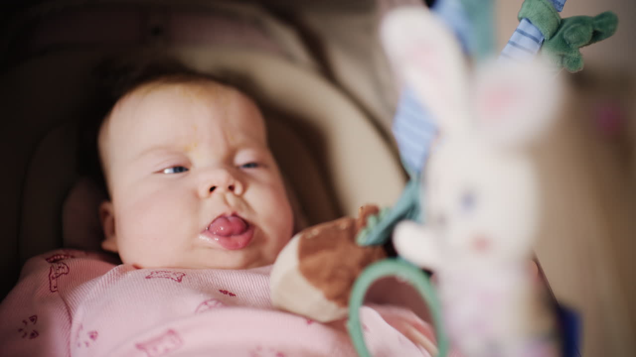 Infant lying on back under a soft baby play gym, looking up at hanging plush toys and a small mirror