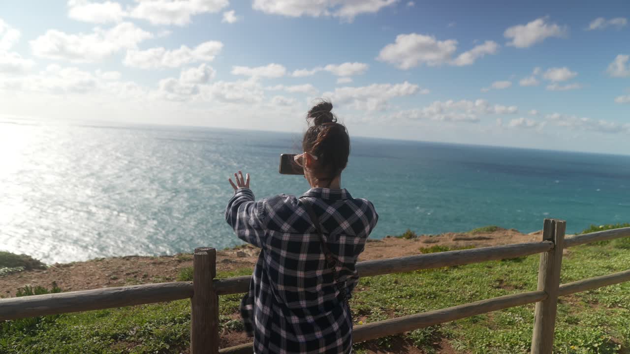 Woman taking a picture of the ocean from a cliff
