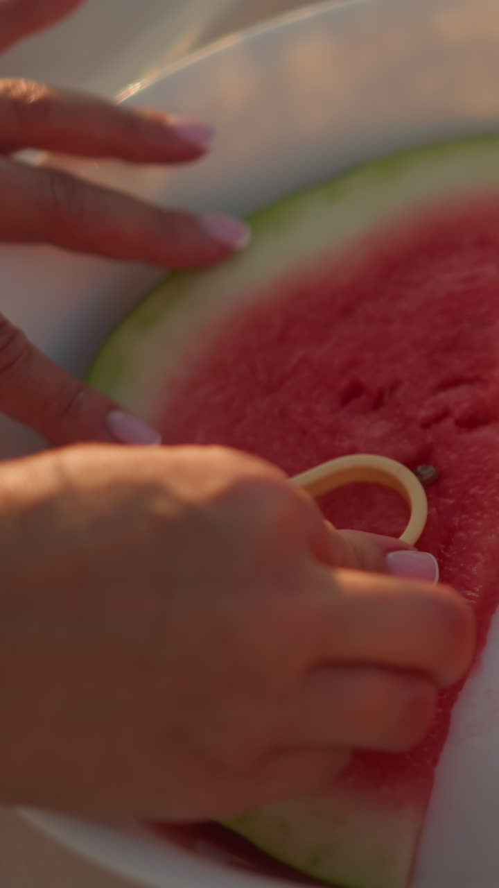 primer plano de la mano presionando un cortador en forma de amor en una jugosa rebanada de sandía en un plato blanco, contrastando la corteza verde y la carne roja vibrante, capturando un momento creativo y lúdico de verano