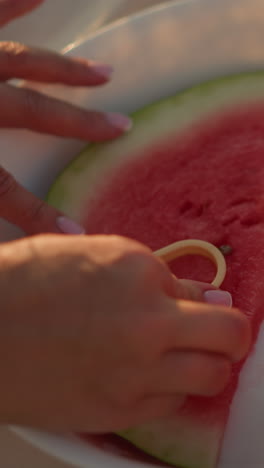 primer plano de la mano presionando un cortador en forma de amor en una jugosa rebanada de sandía en un plato blanco, contrastando la corteza verde y la carne roja vibrante, capturando un momento creativo y lúdico de verano