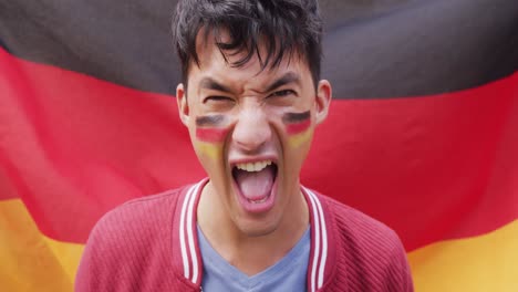 retrato de un feliz hombre biracial con la bandera de alemania en el fondo y en la mejilla