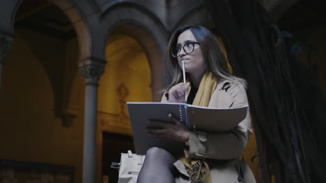 Estudiante-Escribiendo-En-Un-Bloc-De-Notas-En-El-Patio-De-La-Universidad