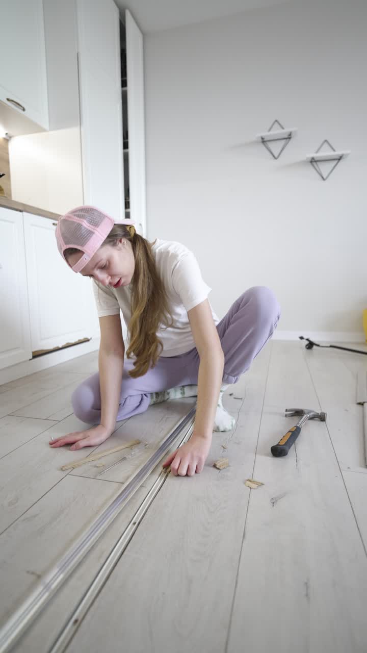 Vertical video shows a woman struggling to fix a floor transition strip by herself, highlighting DIY challenges, home repair effort, and everyday household maintenance indoors