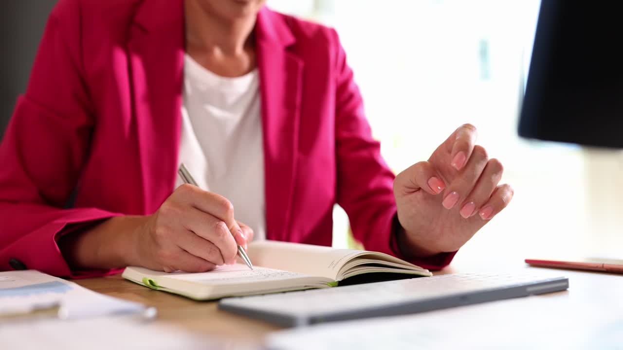 Close-up of a Person Writing in a Notebook and Using a Keyboard at an Office Desk