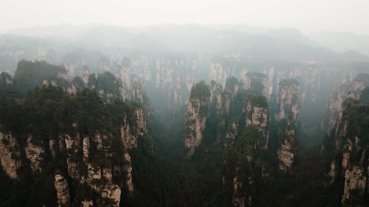 Wide aerial view of forest-covered sandstone pillars stretching across a misty valley in the vast terrain of Zhangjiajie National Park