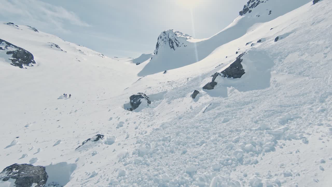 Avalanche debris on pure white mountain slope on sunny day, aerial ascend view