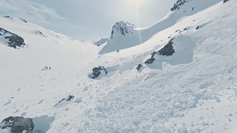 avalanche debris on pure white mountain slope on sunny day, aerial ascend view