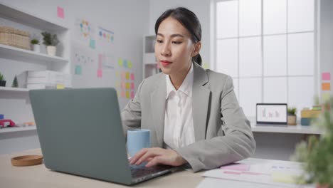 young asia cheerful professional businesswoman finance adviser consultant sitting on desk with laptop computer drink coffee work online at modern office.